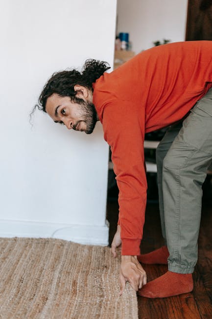 A person using a yellow vacuum cleaner connected to a hose to deep clean a patterned area rug with floral motifs in a residential living room. The rug features soft pastel tones of beige, green, and p